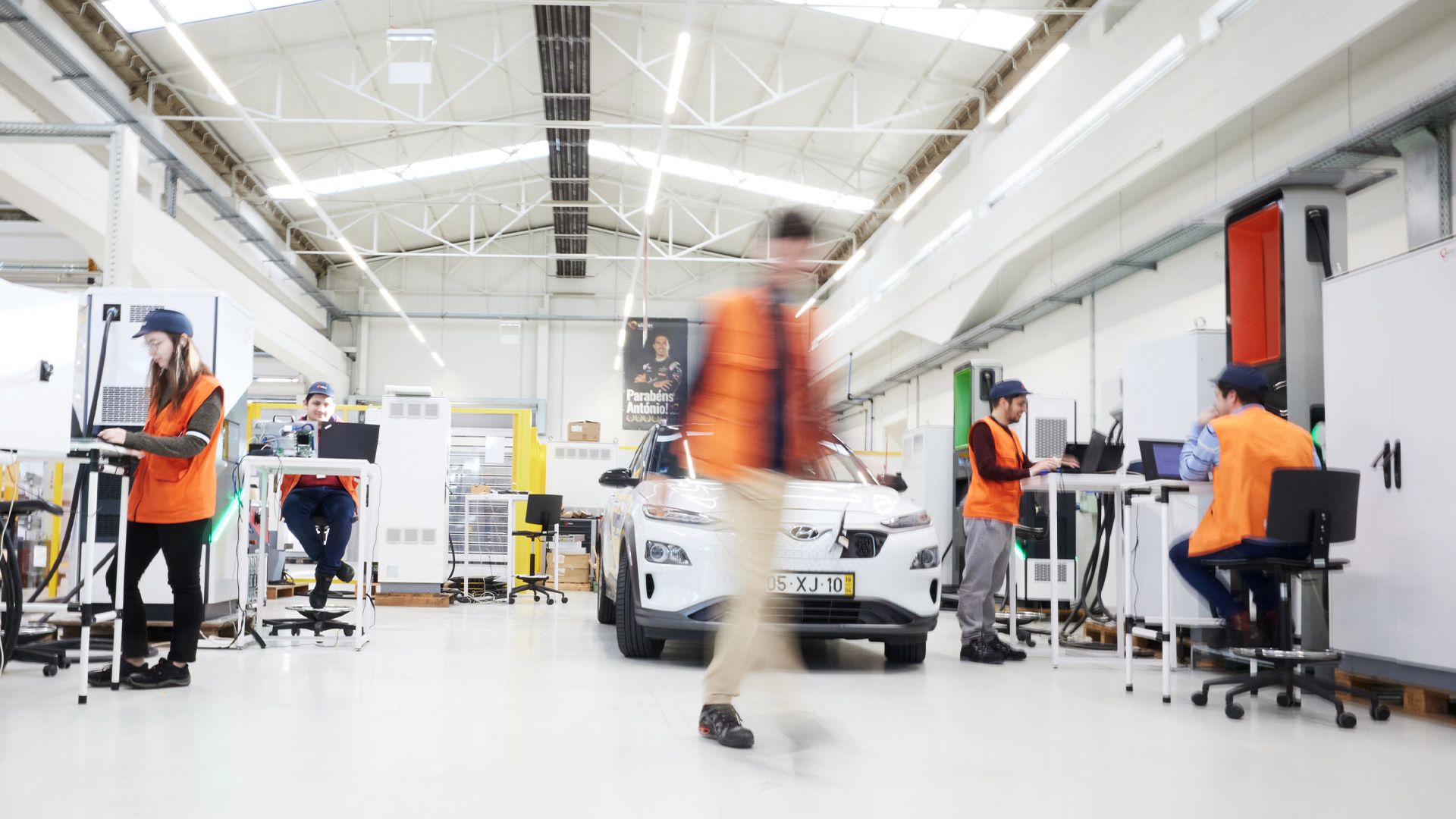 Large and bright electric mobility factory with several workers wearing safety vests.