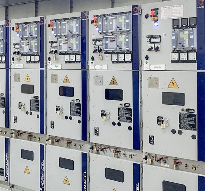 Row of electrical NORMACEL switchgear cubicles with warning signs and control dials.